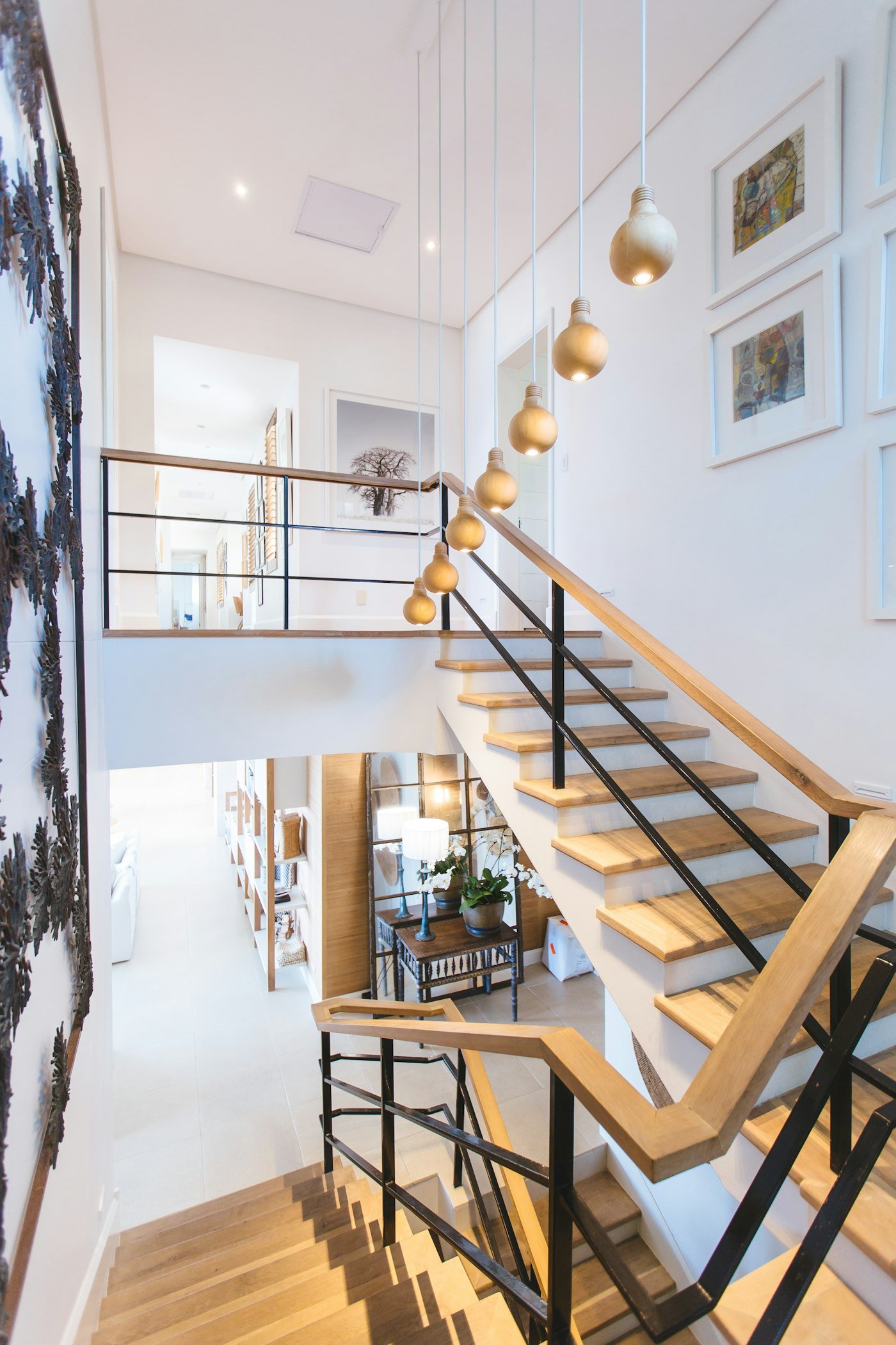 Oak stairs with a black metal rail and a row of wooden bulb lights hanging beside them